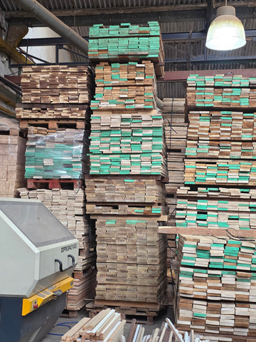 Stacks of wooden planks in a warehouse setting with a machine on the left.